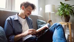 Ein Mann sitzt auf dem Sofa und liest in einem Buch.
