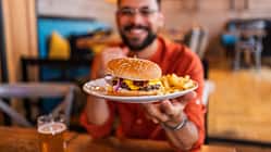 Häufige Ernährungsfehler nach dem Training: Ein sportlicher Mann bekommt einen Teller mit einem Burger und Pommes, auf dem Tisch steht ein Glas Bier.