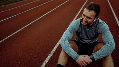 Caucasian male athlete smiling crouching down sitting on tracking field