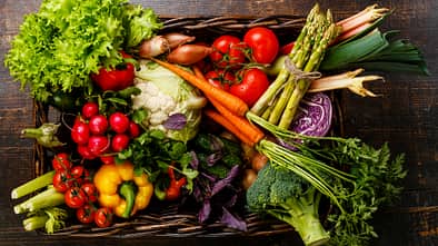 Fresh vegetables in basket on wooden background