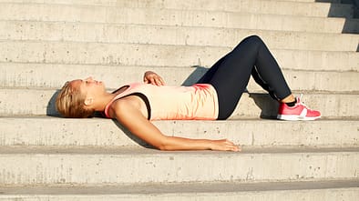 Nachbrenneffekt nach dem Laufen. Eine Läufer liegt auf einer Treppenstufe und erholt sich vom Training.
