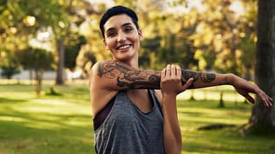 Sport mit Tattoo: Junge Frau mit Tätowierung dehnt sich nach dem Joggen.