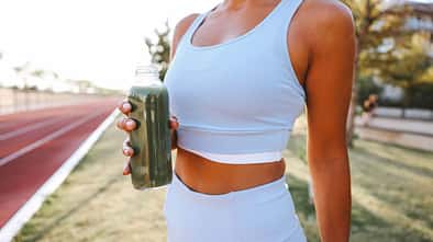 Gesunde Smoothies für Läufer: Nach dem Training auf der Laufbahn hält eine Läuferin eine Flasche mit einem grünen Smootie in der Hand.