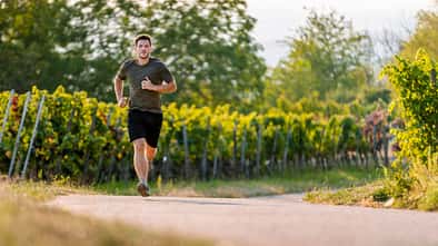 Lauf-Trainingsplan: 5 Kilometer unter 30 Minuten Junger Mann läuft auf einem Weg entlang von Weinstöcken.