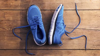 Ein paar blaue Laufschuhe liegen auf einem dunklen Holzfußboden.