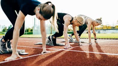 Laufdisziplinen beim Deutschen Sportabzeichen: Drei Läuferinnen hocken in den Startblöcken auf einer Leichtathletikbahn.