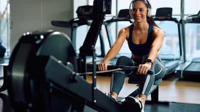 Eine junge Frau trainiert auf einer Rudermaschine im Fitnessstudio.