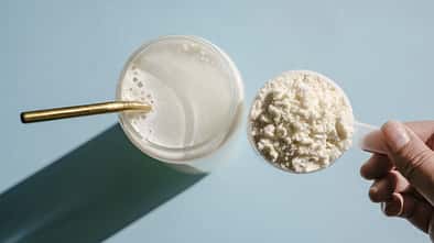 Ein Messlöffel mit Whey-Pulver und ein angerührter Drink in einem Glas mit Strohhalm