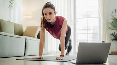 Cardio-Work-out zu Hause: Eine Frau macht Mountain Climber im Wohnzimmer.