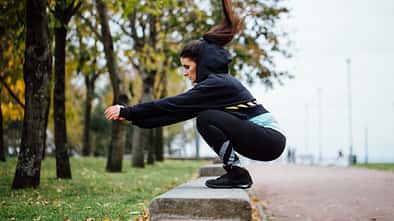 Tabata-Intervalle: Eine Läuferin macht Box-Jumps auf einer Bank im Park.