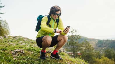 Ein Trailläufer blickt während einer Pause in den Bergen auf seine Laufuhr und sein Smartphone.