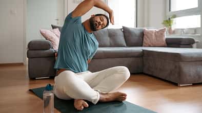 Ein Mann beim sanften Stretching im Wohnzimmer.