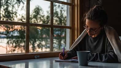 Abendroutine: Eine Frau sitzt mit einer Tasse Tee am Tisch und schreibt in ein Tagebuch.