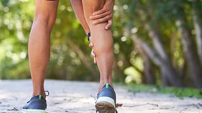 Close up of man holding calf in pain, sports injury trail run, cramp