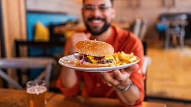 Häufige Ernährungsfehler nach dem Training: Ein sportlicher Mann bekommt einen Teller mit einem Burger und Pommes, auf dem Tisch steht ein Glas Bier.