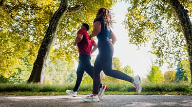 Eine Läuferin und ein Läufer trainieren gemeinsam auf einer Straße durch die Natur.