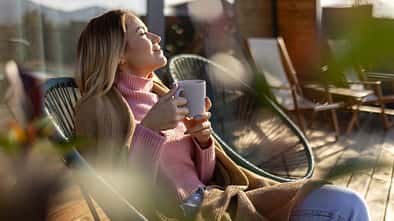 Eine junge Frau entspannt sich mit einer Tasse Tee auf einer Terrasse in der Sonne.