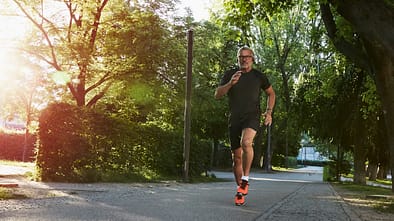 5x5-Intervalle: Ein ambitionierter Läufer trainiert bei Sonnenschein auf einer Straße im Park.