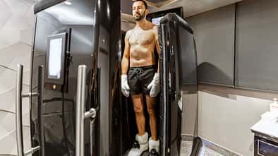 Ein Mann steht mit kurzer Hose, Handschuhen und Plüschschuhen vor einer Kältekammer.