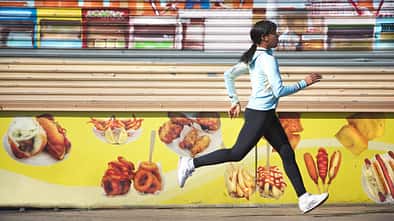 Kalorienverbrauch beim Laufen: Eine Läuferin rennt vor einer Wand mit Essens-Graffiti.
