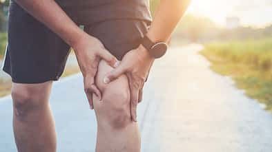 Injury from workout concept : Asian man use hands hold on his knee while running on road in the park. Shot in morning time, sunlight and warm effect with copy space for text or design
