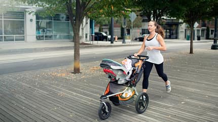 Eine Läuferin schiebt einen Babyjogger, auf dem mit einem Sitzadapter eine Babyschale befestigt wurde. Laufen mit Kinderwagen mit Sitzadapter und Babyschale