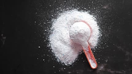Washing powder in plastic spoon on black background top view,Romania