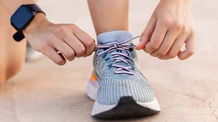 Nahaufnahme von zwei Händen, die einen Laufschuh binden. Am Handgelenk trägt die Person eine Fitnessuhr. Nahaufnahme von zwei Händen, die einen Laufschuh binden. Am Handgelenk trägt die Person eine Fitnessuhr.