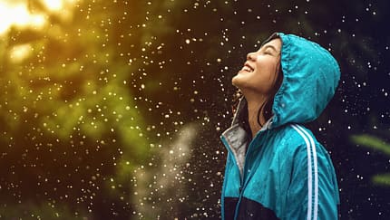 Laufmotivation bei jedem Wetter: Junge Läuferin steht mit einer Regenjacke glücklich im Regen.