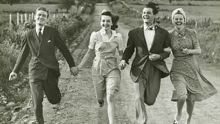Two couples holding hands, running on footpath, (B&W)