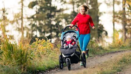 Joggen nach Kaiserschnitt: Laufende Mutter mit ihrem Kind in einem Babyjogger