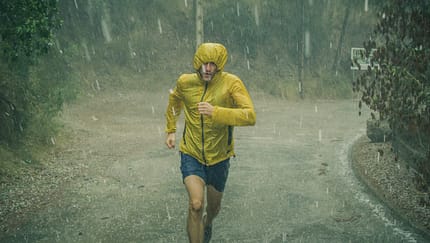 Mann in Regenjacke läuft durch strömenden Regen.