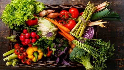 Fresh vegetables in basket on wooden background