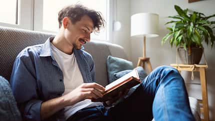 Ein Mann sitzt auf dem Sofa und liest in einem Buch.