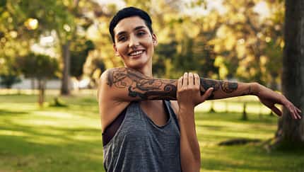Sport mit Tattoo: Junge Frau mit Tätowierung dehnt sich nach dem Joggen.