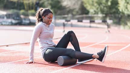 Regeneration im Lauftraining: Eine Läuferin rollt ihre Beinmuskulatur auf einer Faszienrolle aus.