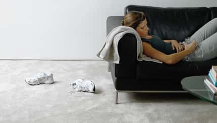 Woman wearing sports clothes resting on sofa, holding drink