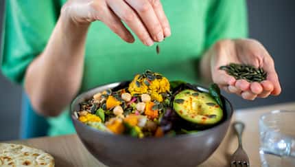 Eine Frau streut Kürbiskerne über ihre Bowl mit Gemüse.