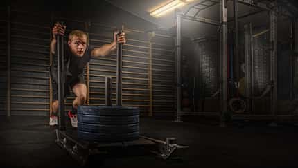 Ein Mann schiebt im Studio schwere Gewichte auf einem Schlitten: Kraftaufbau mit Cross-Training für eine Hyrox-Challenge.