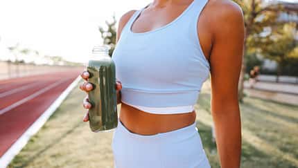 Gesunde Smoothies für Läufer: Nach dem Training auf der Laufbahn hält eine Läuferin eine Flasche mit einem grünen Smootie in der Hand.