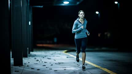 Eine junge Läuferin joggt in der Dunkelheit.