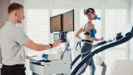 Ein Mediziner führt bei einer Läuferin auf dem Laufband eine Spiroergometrie durch. Die Läuferin trägt eine Atemmaske.