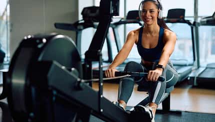 Eine junge Frau trainiert auf einer Rudermaschine im Fitnessstudio.