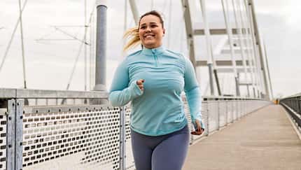 Glückliche Plus-Size-Läuferin läuft auf einer Brücke.
