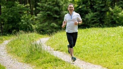 Ein Mann mittleren Alters joggt auf einem Feldweg.