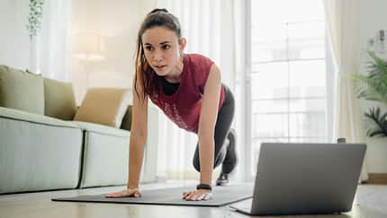 Cardio-Work-out zu Hause: Eine Frau macht Mountain Climber im Wohnzimmer.
