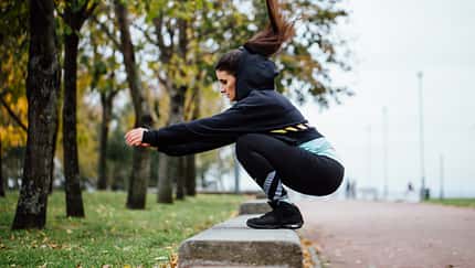 Tabata-Intervalle: Eine Läuferin macht Box-Jumps auf einer Bank im Park.