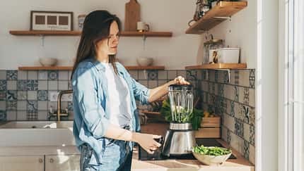 Eine Frau mixt sich mit einem Smoothiemaker einen grünen Smoothie.