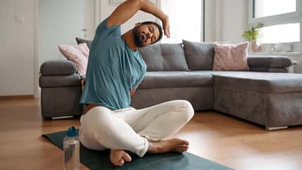 Ein Mann beim sanften Stretching im Wohnzimmer.