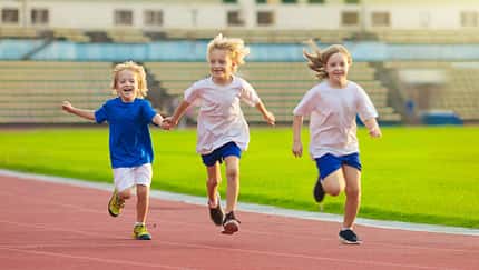 Drei Kinder laufen zusammen auf einer Laufbahn im Stadion.